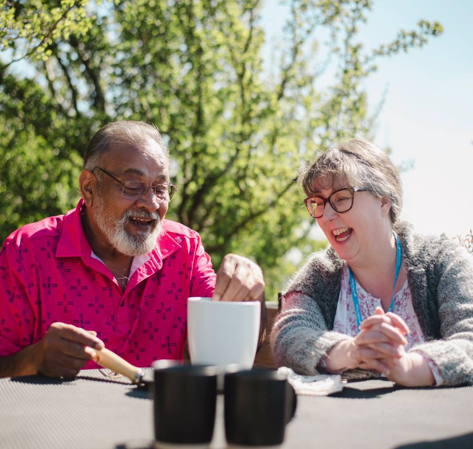 Caregiver and elderly man sharing tea outdoors.