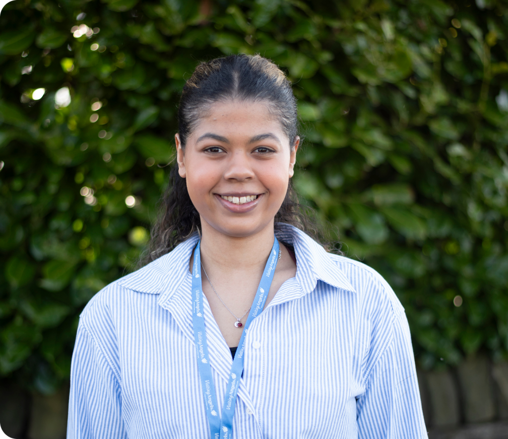 Smiling female caregiver standing against greenery.